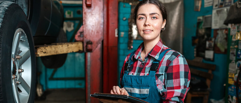 Frau mit Tablet am Auto auf Hebebühne
