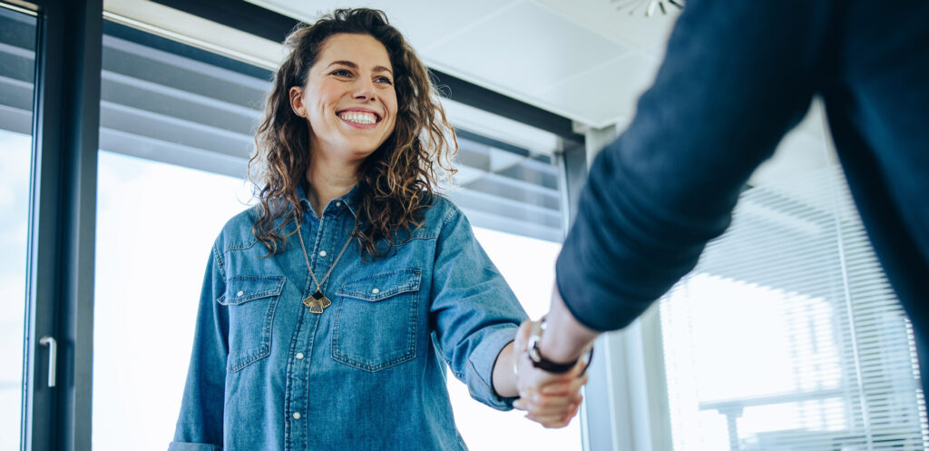 Junge, dunkelhaarige Frau schüttelt einem Chef die Hand